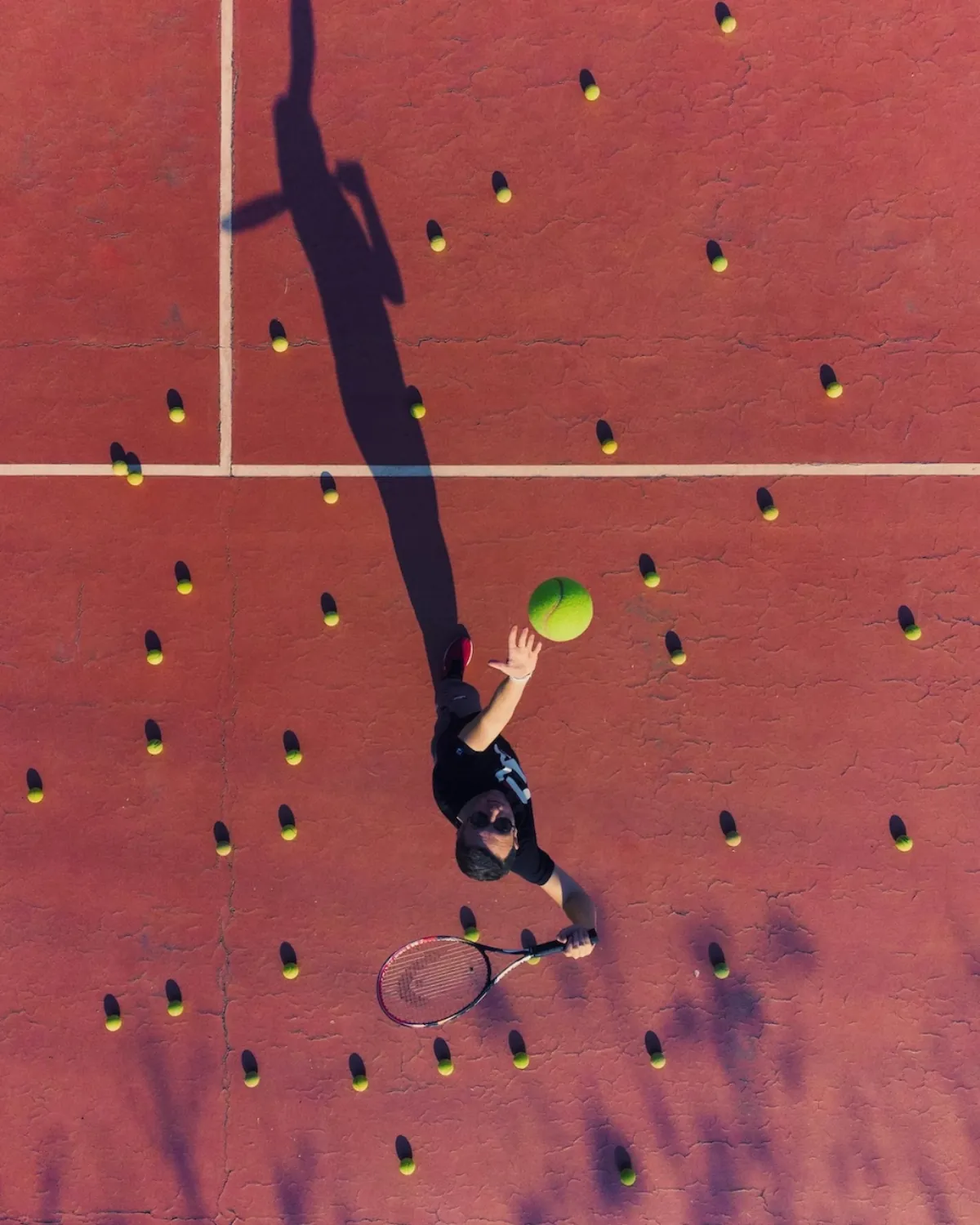 Overhead view of a tennis player on court surrounded by scattered balls